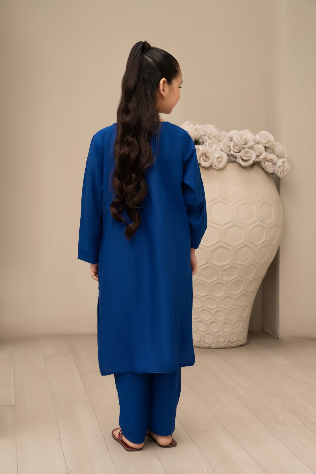 Girl wearing a blue outfit standing next to a large decorative vase with a floral design.