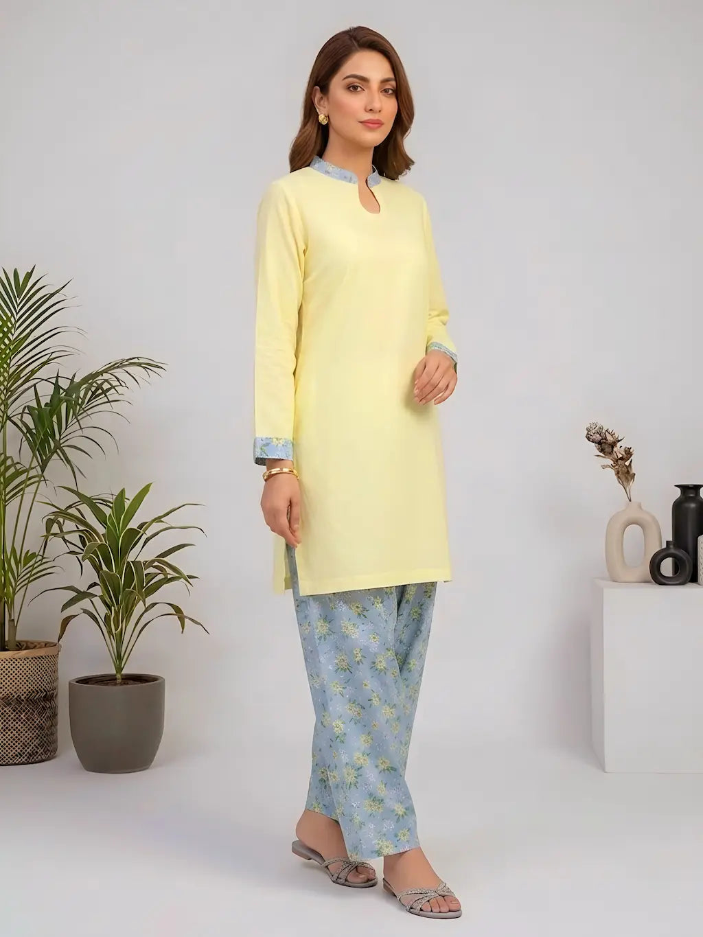 Woman wearing a light yellow kurta with blue floral shalwar in a minimalistic setting.