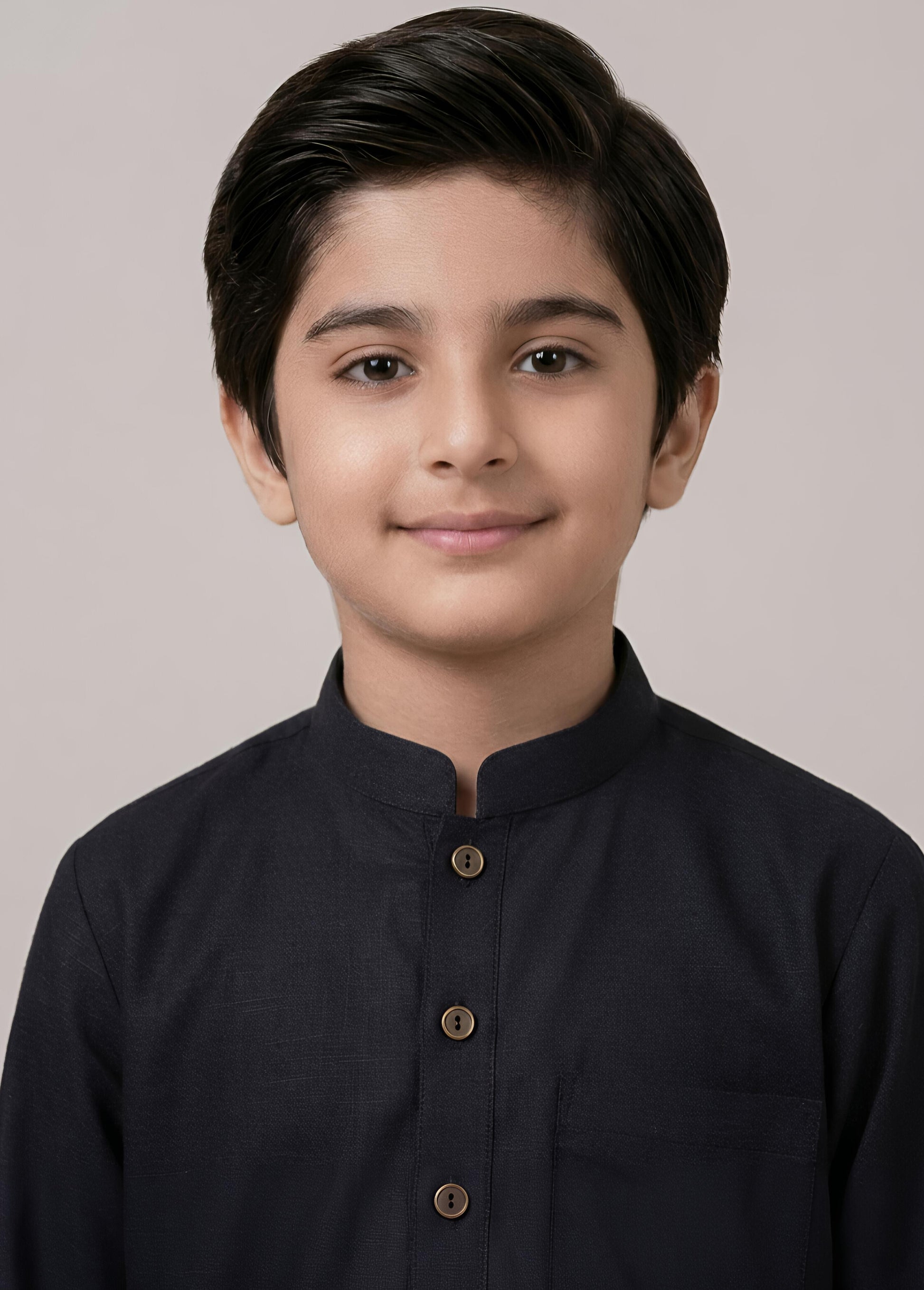 Young boy wearing a black kurta against a plain background