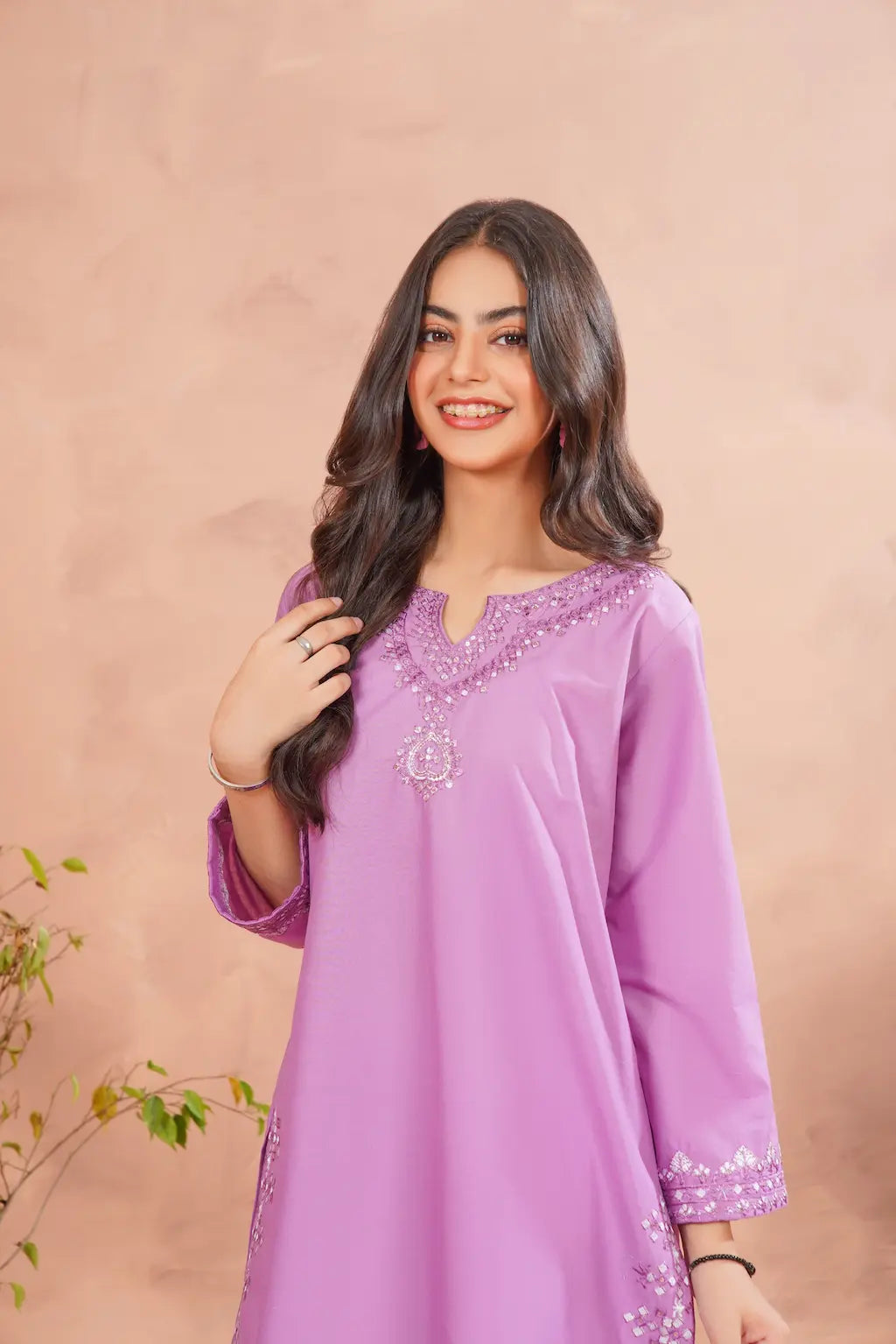Woman wearing a purple dress with floral embellishments against a beige background