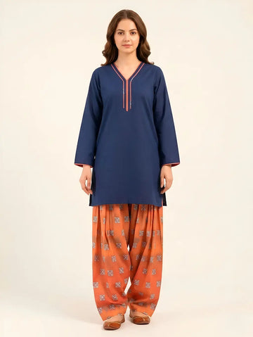 A woman posing in a navy blue short-length lawn tunic with coral-pink piping on the V-neckline and cuffs, paired with a voluminous, digital-printed rust Farshi shalwar and traditional brown flats.