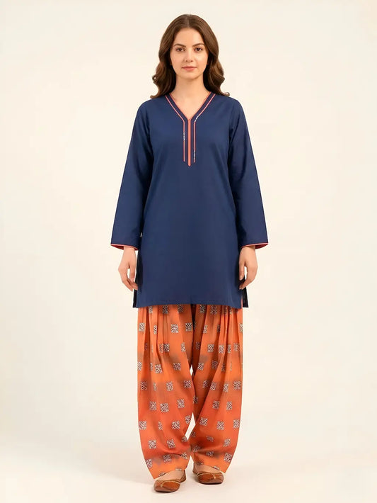 A woman posing in a navy blue short-length lawn tunic with coral-pink piping on the V-neckline and cuffs, paired with a voluminous, digital-printed rust Farshi shalwar and traditional brown flats.