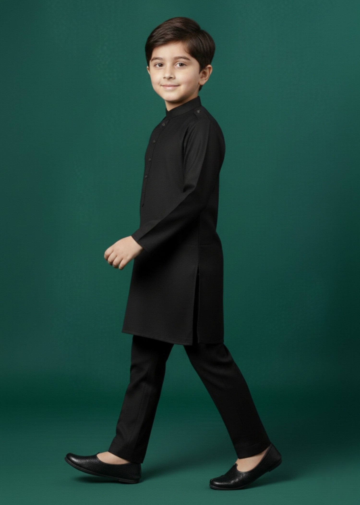 Young boy wearing a black kurta with black shoes on a green background