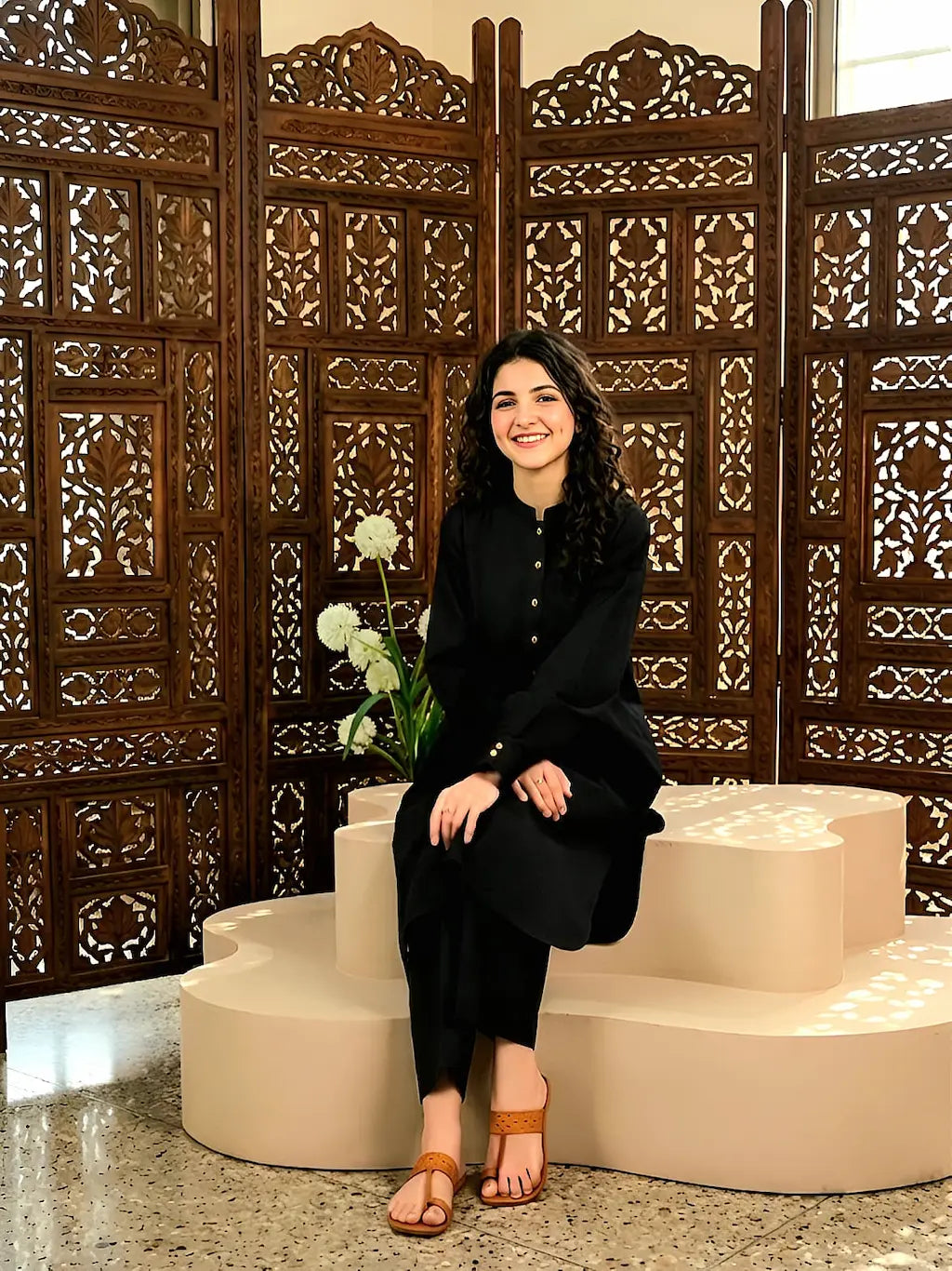 A girl in black outfit sitting on steps with decorative wooden screen in background