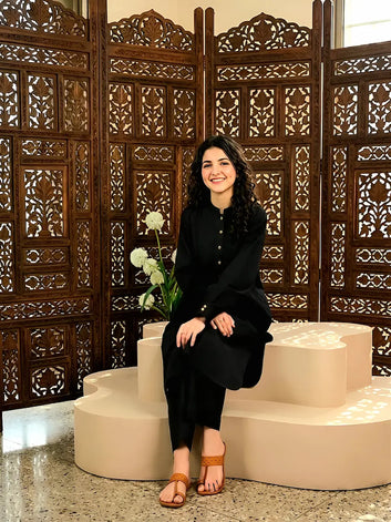 A girl in black outfit sitting on steps with decorative wooden screen in background