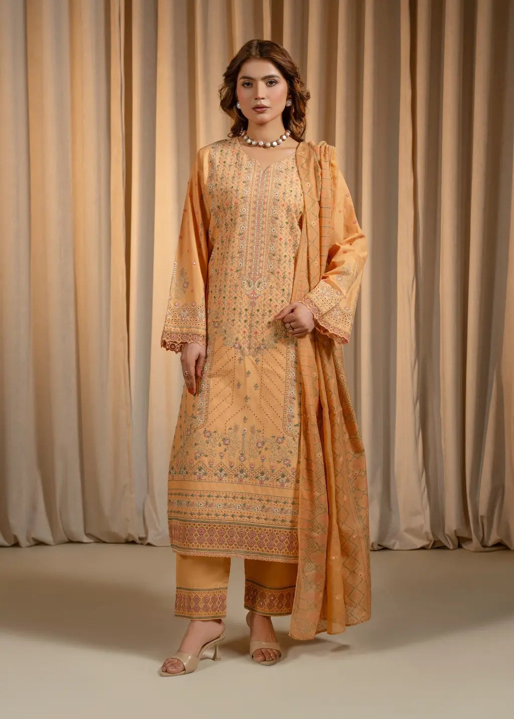 Woman wearing a traditional outfit with intricate patterns against a beige curtain background