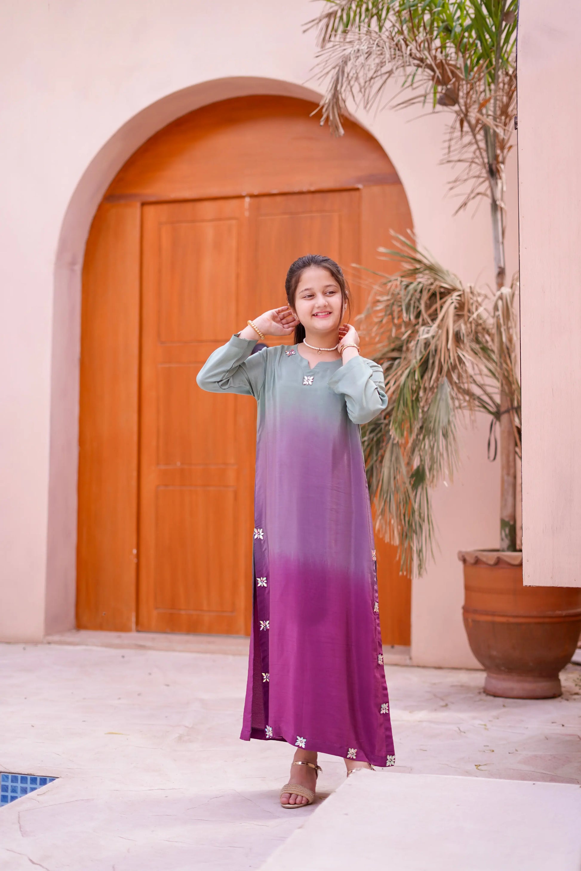 Girl wearing a gradient dress standing in front of a wooden door.