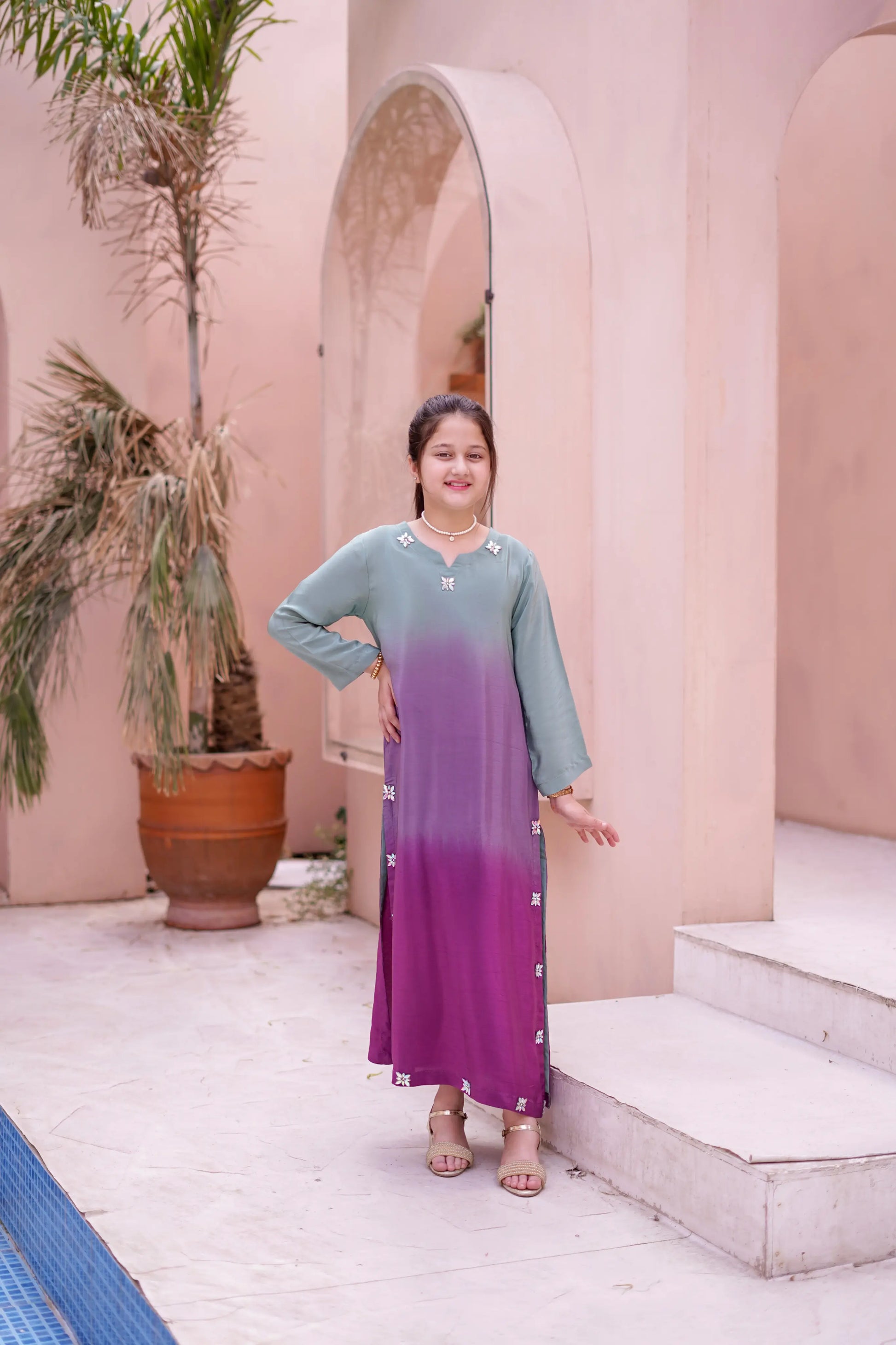 Girl in a gradient dress standing in front of a pink wall with arches