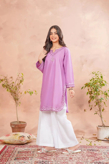 Woman wearing a purple top and white pants against a beige background with plants.