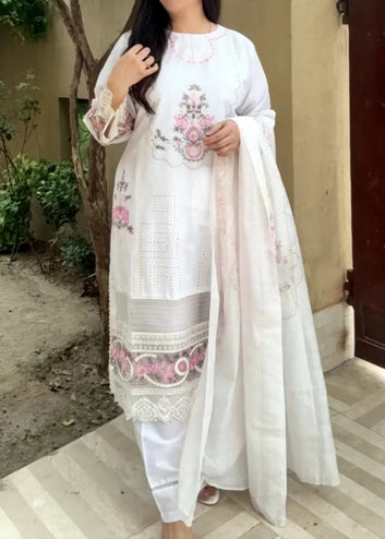 Woman wearing a white embroidered outfit with a long white scarf outdoors.