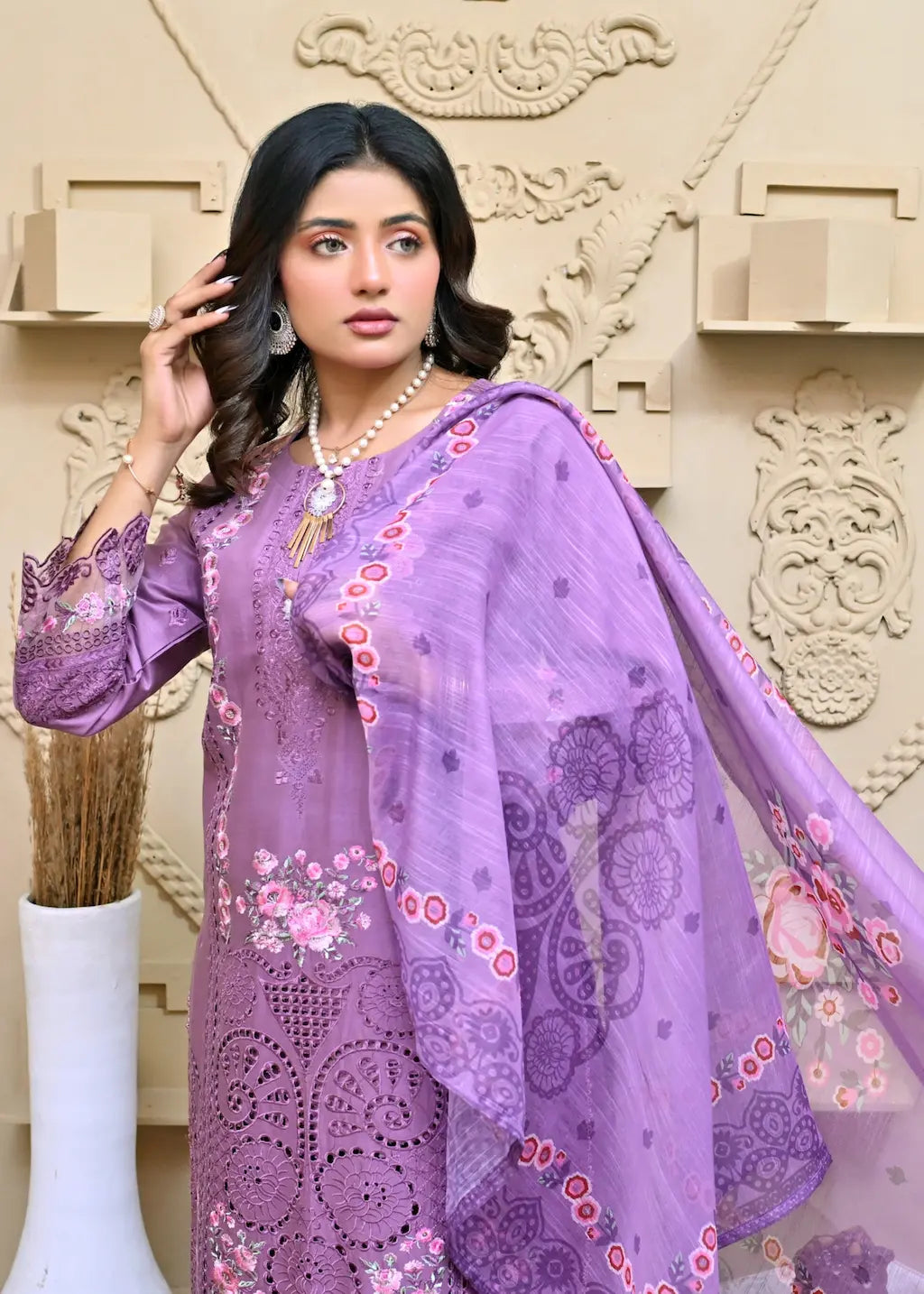 Woman wearing a purple embroidered outfit with a matching dupatta against an ornate wall.