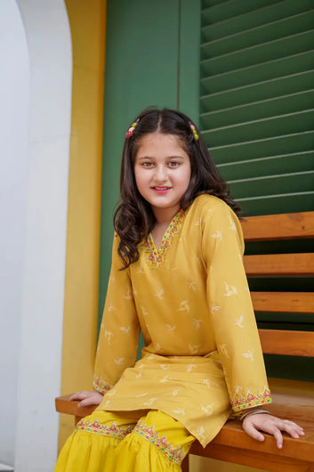 Young girl in a yellow traditional outfit sitting on a wooden bench.