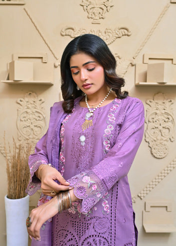 Woman in a purple embroidered outfit standing against an ornate wall.