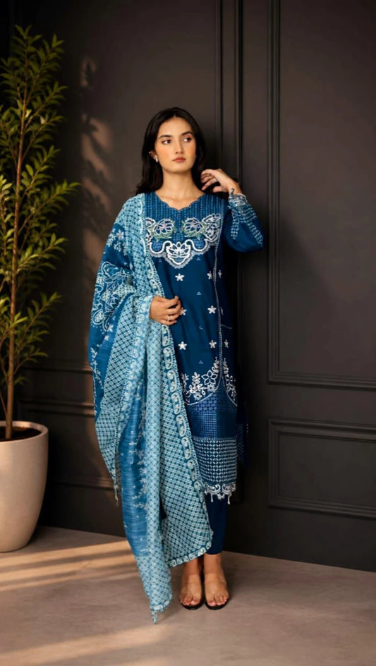 Woman wearing a teal blue traditional outfit with white embroidery against a dark wall.