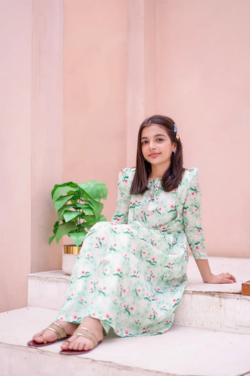 Young girl in a floral dress sitting on steps with a pink wall and plant in the background
