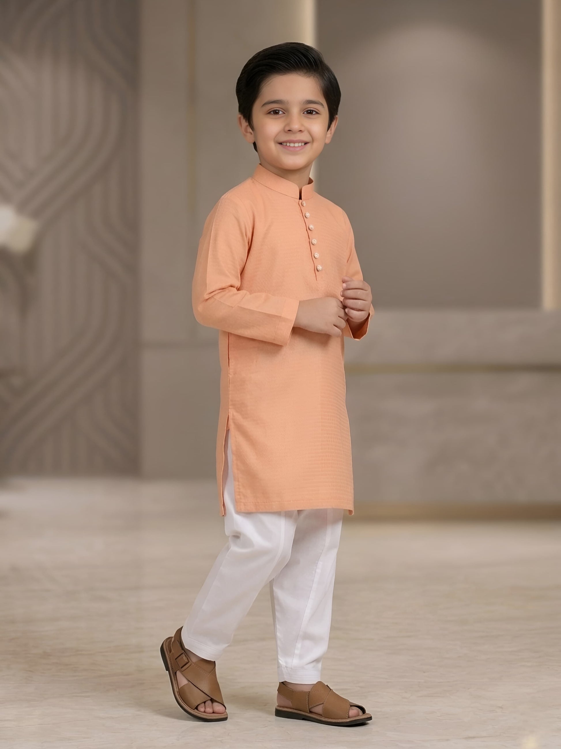 Young boy wearing an orange kurta with white pants against a neutral background