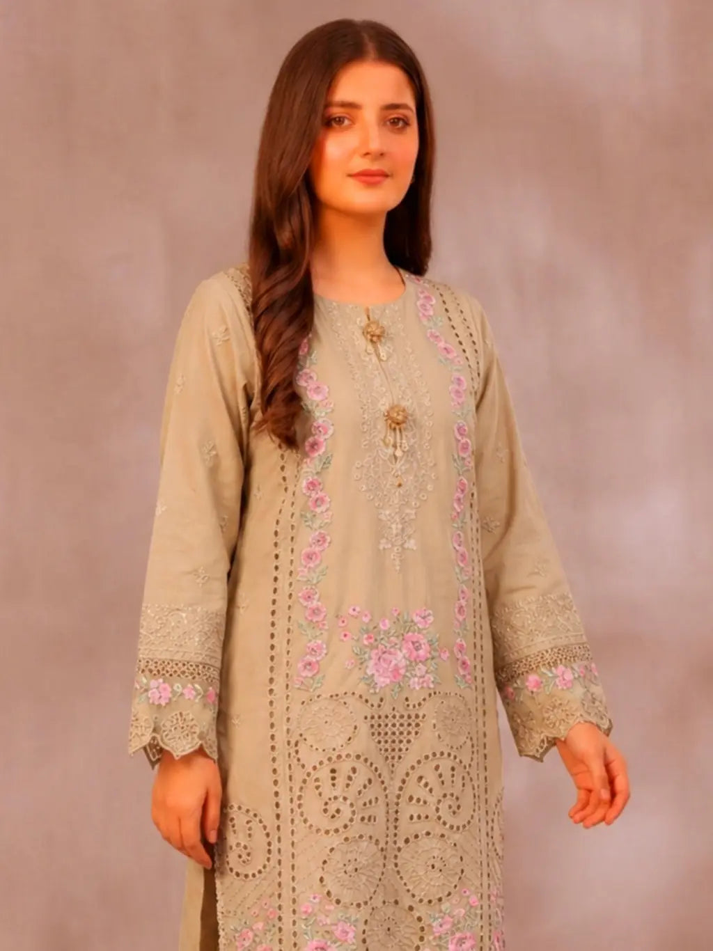 Woman wearing a beige embroidered dress with pink floral patterns against a plain background
