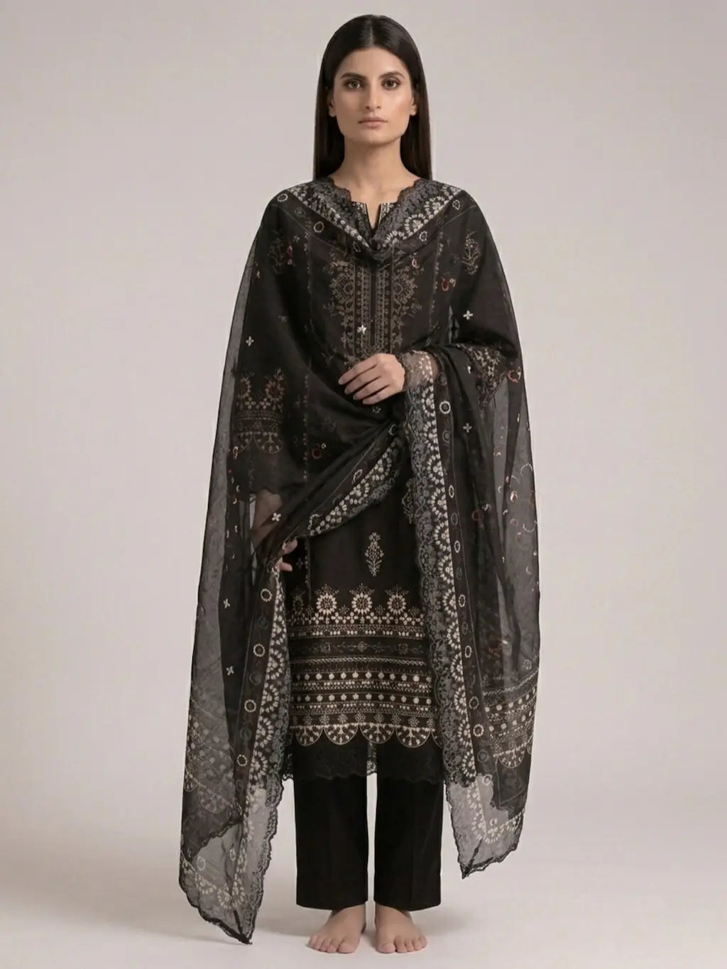 Woman wearing a black and patterned traditional outfit with a sheer dupatta on a plain background