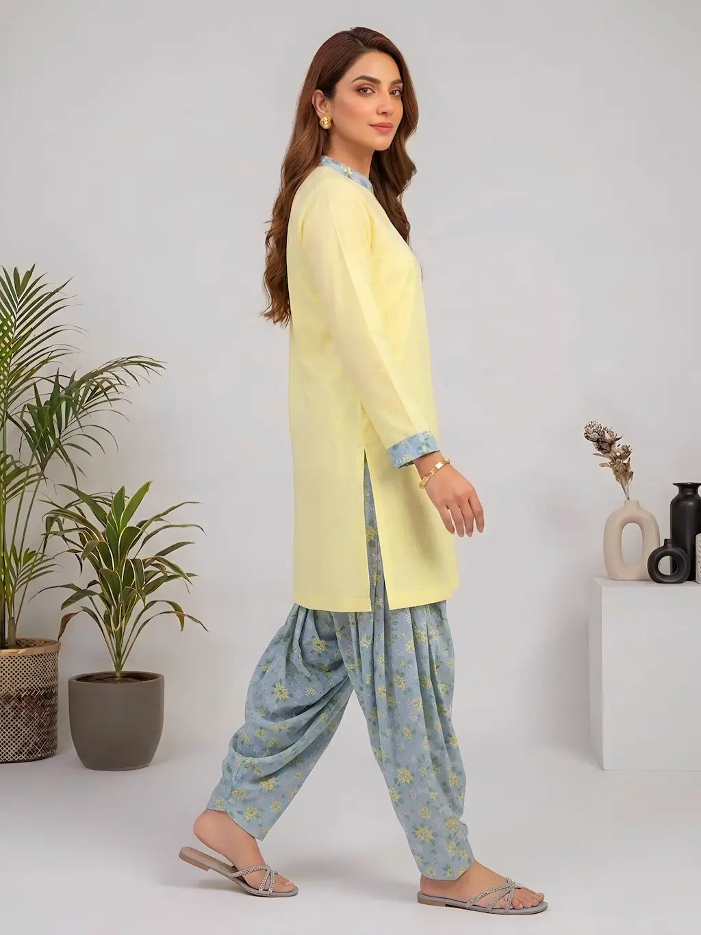 Woman wearing a light yellow kurta with blue floral shalwar in a minimalistic setting.