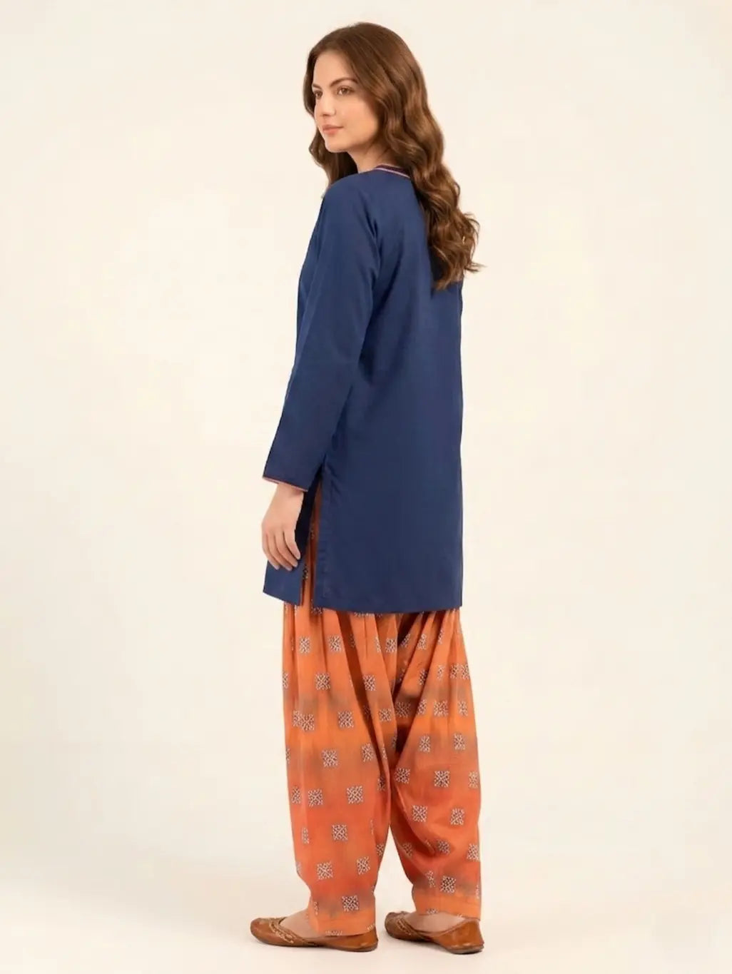 Rear three-quarter view of a navy blue lawn shirt in a short length, paired with a digital printed rust-orange Farshi shalwar, highlighting the drape and voluminous silhouette.