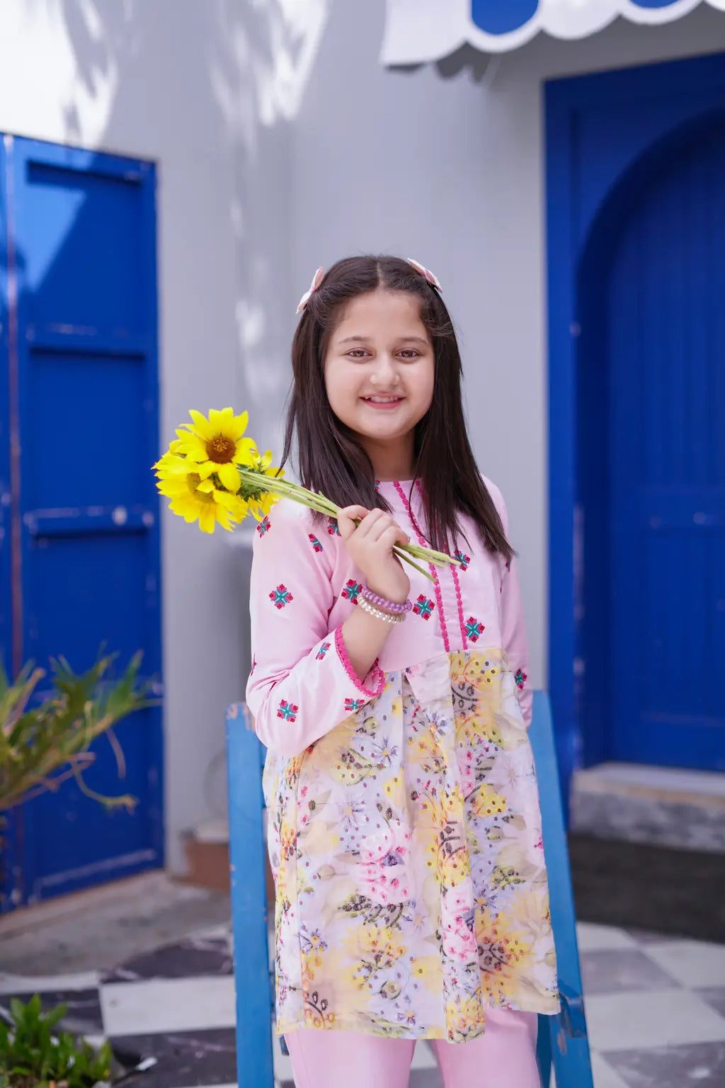 Young girl holding a sunflower in front of a blue door and white wall.