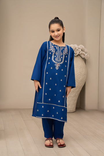 A child wearing a blue embroidered cotton shirt and trouser, standing in a room with light-colored walls and a sculpture in the background.